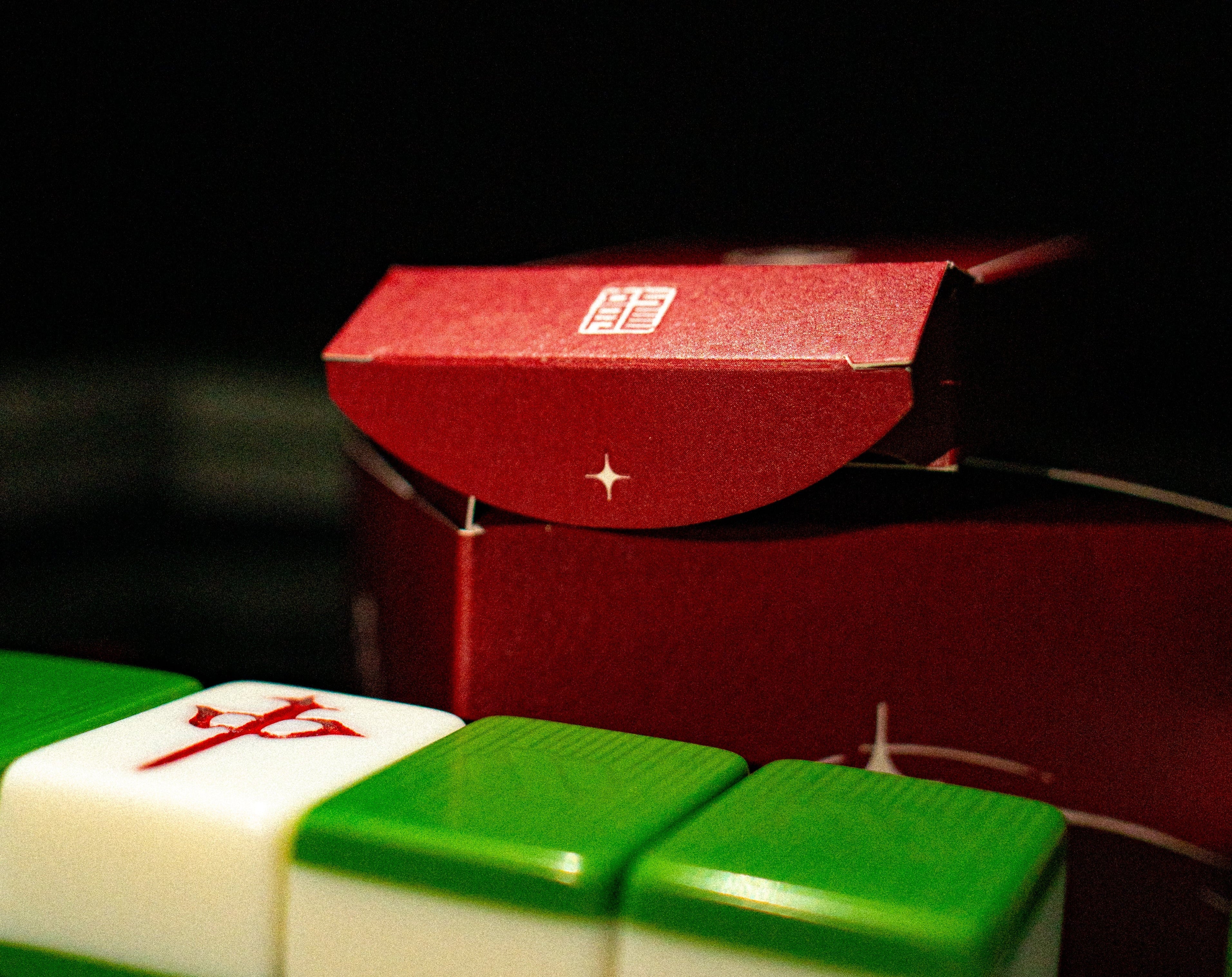 Red mahjong box with green and white tiles on a dark background